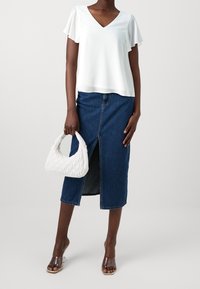 Vit kortärmad T-shirt med V-ringning, denim midi kjol med sprund fram, klara klacksandaler och en vit vadderad handväska.