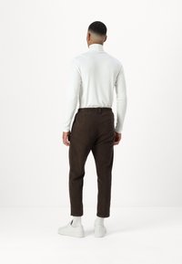 Hvit langermet høyhalset genser kombinert med brune kordfløyelsbukser og hvite joggesko, som viser en avslappet passform og elastisk midje.