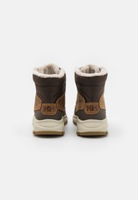 Bottes isolées marron avec une tige texturée, un col en fourrure et une semelle en caoutchouc. Présente des accents de marque en cuir sur le talon.