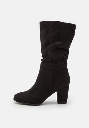 Botín negro de ante, con un diseño holgado y un tacón grueso. Presenta una puntera redondeada y un sutil detalle del logo en el tacón.