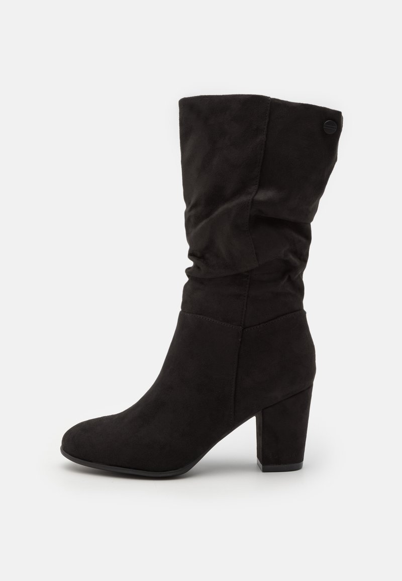 Stivaletto slouchy nero realizzato in suede con un tacco spesso. Presenta una punta arrotondata e un sottile dettaglio del logo sul tacco.