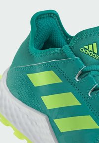 Chaussure de sport turquoise avec une tige en mesh, trois rayures vert lime bien visibles et une semelle en caoutchouc blanc texturé.