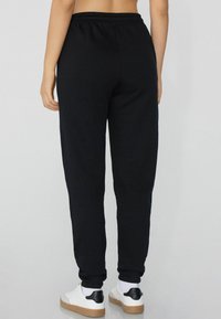 Schwarze Baumwoll-Sweatpants mit einem elastischen Bund, schmal zulaufenden Beinen und Bündchen. Kombiniert mit weißen Sneakers mit schwarzen Akzenten.