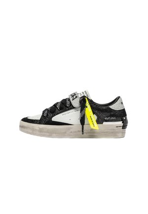 Sneaker in bianco e nero con tomaia testurizzata, suola liscia, dettagli riflettenti, lacci neri e un'etichetta gialla brillante.