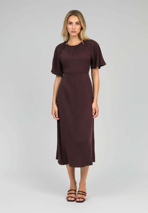 Robe midi mauve à manches courtes, avec un détail au col plissé, en tissu doux et à silhouette évasée. Associée à des sandales à lanières brunes.