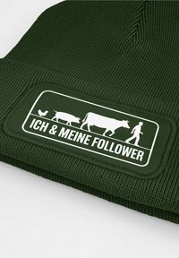 Green knitted beanie featuring a textured, ribbed design. A white rectangular patch displays a graphic of animals and the text "ICH & MEINE FOLLOWER."