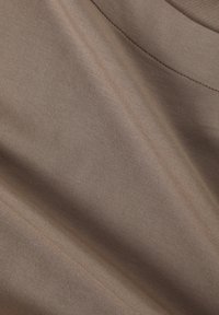 Tissu marron clair avec une texture douce et lisse, présentant un léger côtelé et des plis délicats, indiquant une flexibilité et une qualité de drapé.
