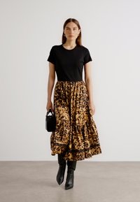 T-shirt nera e una gonna a strati con stampa leopardata in beige e marrone, abbinata a stivali neri al ginocchio e a una piccola borsa nera.