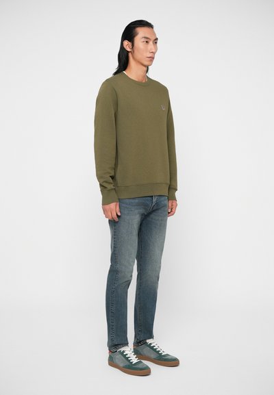 Un sweat-shirt olive à col ras du cou avec des poignets côtelés, assorti à un jean bleu clair et des baskets multicolores avec un motif.