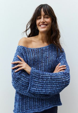 Blå stickad tröja med en lös, texturerad design och vida ärmar. Har en off-shoulder stil och ett öppet stickmönster.