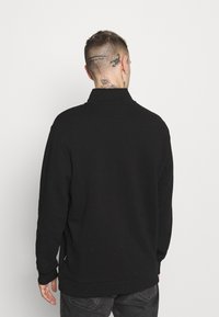 Zwarte sweatshirt van zachte stof, met een hoge kraag en lange mouwen. De zoom en manchetten zijn geribbeld, met een ontspannen pasvorm.