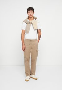 Pantalons cargo beiges avec poches latérales, associés à un t-shirt blanc à manches courtes et une écharpe tricotée beige clair drapée autour du cou.