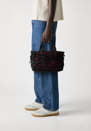 Zwarte tas met rode accenten, textured materiaal en geweven ontwerp. Beschikt over korte handvatten en de tekst "VOOR EEN SUCCESVOL LEVEN" op de bodem.