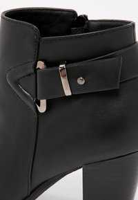 Black leather ankle boot with a rounded toe, silver hardware detail on the side, and a chunky textured heel. Smooth exterior finish.