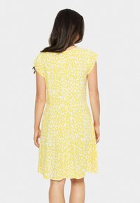 Robe jaune avec imprimé léopard blanc ; manches courtes, corsage ajusté et jupe évasée. Tissu léger, texture lisse.