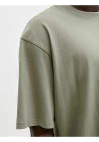 Koszulka z krótkim rękawem i okrągłym dekoltem w jasnym oliwkowym kolorze, wykonana z bawełny. Charakteryzuje się luźnym krojem, gładką teksturą i starannym wykończeniem brzegów.