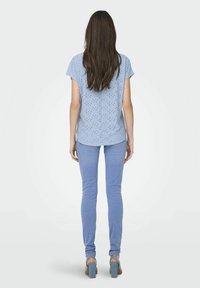 Lyseblå kortærmet top med perforeret design, parret med lyseblå skinny jeans og blå hæle-sandaler. En simpel og tætsiddende silhuet.