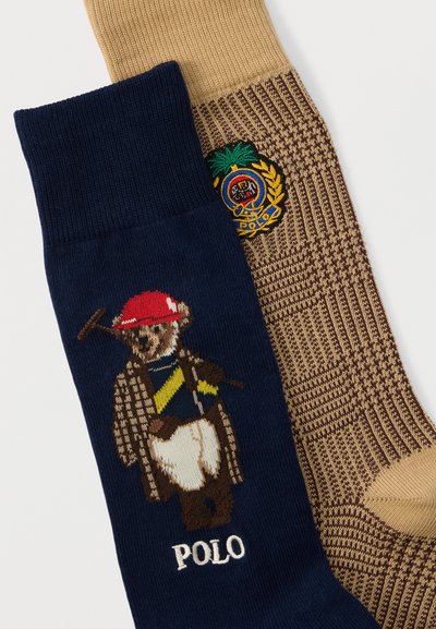 Ζευγάρι κάλτσες, η μία μπλε σκούρη με μία αρκούδα που φοράει ρουχισμό πόλο και τη λέξη "POLO", η άλλη μπεζ και καφέ με ένα πολύχρωμο κεντημένο έμβλημα.