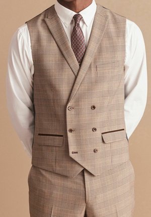 Homme portant un gilet croisé à carreaux beige avec un pantalon assorti, une chemise blanche et une cravate marron à motifs sur un fond neutre.