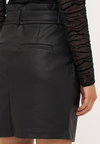 Μαύρη δερμάτινη φούστα με απαλή υφή, ζώνη στη μέση και δύο πίσω τσέπες. Ο σχεδιασμός είναι κομμένος για στενή εφαρμογή.