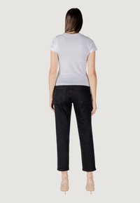 Witte t-shirt met korte mouwen in combinatie met op maat gemaakte zwarte jeans. De jeans hebben zakken en een rechte pasvorm. Neutrale achtergrond.
