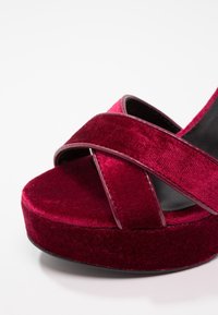Sandale plateforme en velours rouge avec lanières croisées et semelle intérieure noire sur fond blanc.