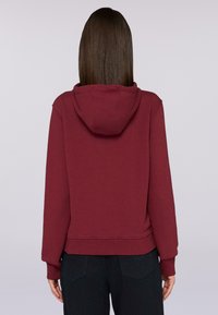 Sudadera con capucha burdeos hecha de un tejido suave; presenta puños y dobladillo acanalados, con un corte relajado y sin marcas visibles.