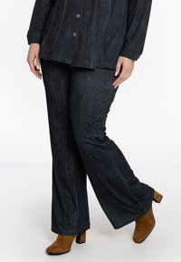 Donkerdenim wijde broek met subtiele verticale textuur, gecombineerd met een bijpassende button-up top. Bruine enkellaarsjes maken de outfit compleet.