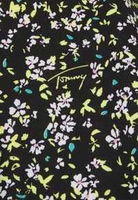 Czarna tkanina z kwiatowym wzorem w bieli, różu i żółci, z zielonymi akcentami. Zawiera charakterystyczny napis "Tommy" w kursywie.