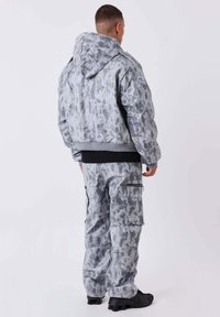Grijze tie-dye bomberjack met een capuchon, ribgebreide manchetten en bijpassende cargobroek met zijzakken en ritsdetails.