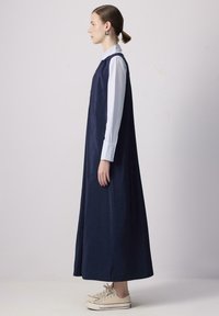 Vestido maxi azul marino con un corpiño ajustado y una silueta holgada, que presenta una camisa blanca con cuello debajo y zapatillas de lona.