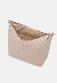 Sac à main matelassé beige avec fermeture éclair dorée et logo triangulaire Guess, montrant la doublure intérieure beige avec petite poche zippée et nom de la marque imprimé.