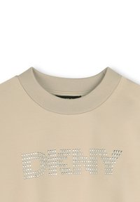Sudadera beige con cuello redondo y puños acanalados, que presenta un diseño de tachuelas que deletrea "DENY" en la parte frontal. Textura de tela suave.
