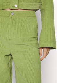 Groene corduroy cropped jacket en high-waisted broeken, met verticale strepen, drukknopen en een zachte textuur.