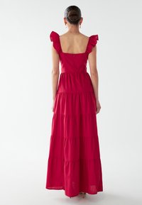 Robe maxi rouge longue avec des manches volantes, un décolleté carrée, un design à superpositions et une fermeture éclair au dos. Texture de tissu lisse.