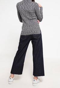 Grauer strukturierter Langarmtop kombiniert mit dunkelblauen weiter geschnittenen Jeans. Weiße Sportschuhe mit schwarzen Akzenten. Der Saum der Jeans ist ausgefranst.