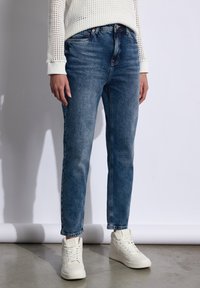 Jeans de mezclilla azul claro con corte recto, diseño de cinco bolsillos y un acabado desgastado, combinados con zapatillas altas blancas.