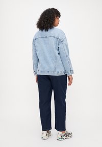 Chaqueta de mezclilla azul claro con un corte holgado, costuras visibles y detalles de botones, combinada con pantalones azul oscuro y zapatillas deportivas.