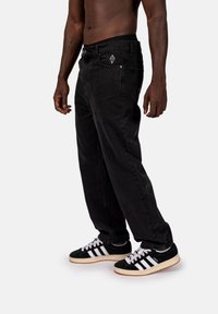 Svarta denimjeans med avslappnad passform, med en framtagen ficka och en diamantlogotyp nära midjan. Matchas med svartvita sneakers.