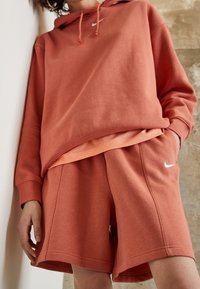 Rust-colored Nike hoodie with a front pocket and drawstring hood paired with matching shorts. Soft fabric, relaxed fit, minimalistic branding.