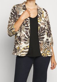 Blazer med blomsterprint i creme med nuancer af brunt og gult, i en afslappet pasform og med trekvartlange ærmer. Bæres over en sort top.