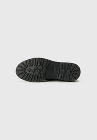 Black rubber shoe sole with textured traction pattern and logo detail. Rounded shape designed for grip and stability.