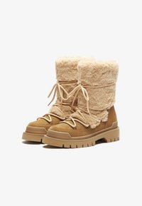 Botas forradas de piel en un tono marrón claro, con parte superior acolchada, cierre de cordones y suela de goma gruesa. Suave textura y altura distintiva que mejoran la calidez y la comodidad.