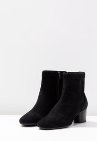 Bottes à chevilles en suède noir avec un bout arrondi, une fermeture éclair latérale et un talon épais. Texture douce et design lisse.