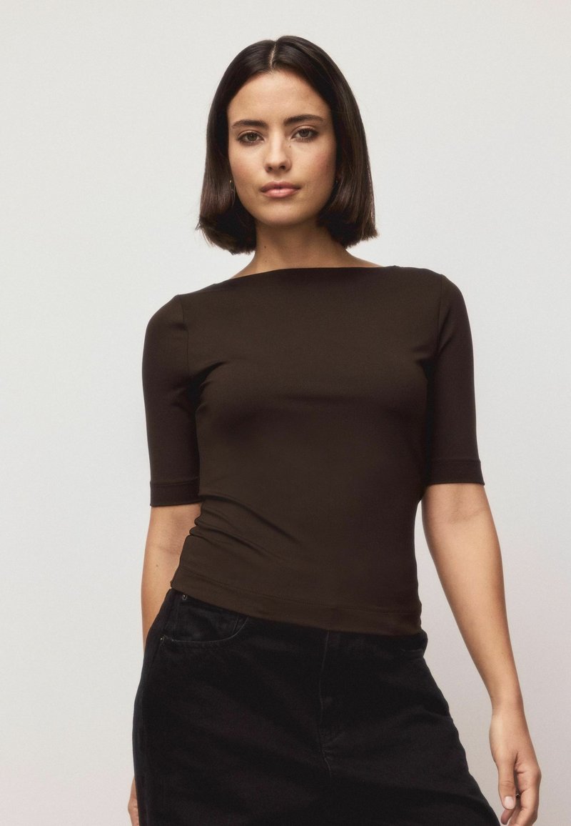Brown fitted top with short sleeves, round neckline, and smooth texture. Paired with black pants, creating a sleek silhouette.