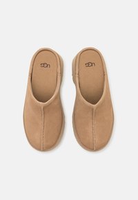 Paire de chaussons en daim couleur beige avec bout rond et coutures apparentes, vus de dessus sur un fond blanc.
