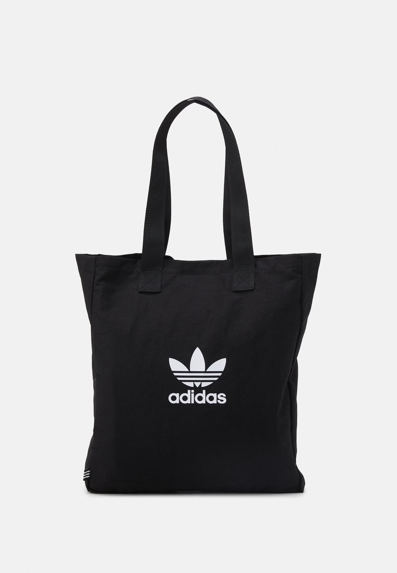 Černá taška přes rameno s dlouhými popruhy, která má uprostřed na přední části bílou trefoil logo Adidas na čistém pozadí.