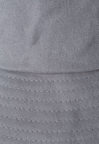 Gråt stofhat med en struktureret overflade og syede detaljer omkring skyggen, som har en klassisk kasketform og flad profil.