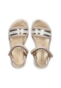 Sandalias metálicas doradas y beige con dos correas anchas, hebilla en el tobillo y suela blanca. Plantilla texturizada con el nombre de la marca grabado.