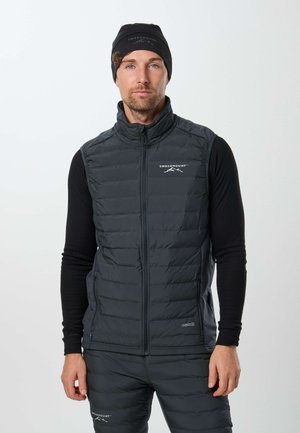 Homme portant un bonnet noir Swedemount, une chemise noire à manches longues, un gilet matelassé noir et un pantalon matelassé noir assorti, debout devant un fond blanc.
